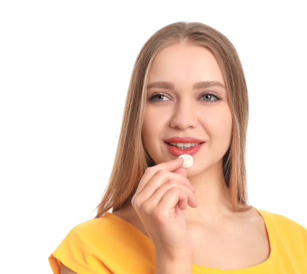 istock Young woman taking vitamin pill on white background 1336652716