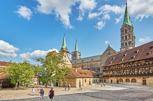 Bamberg, Germany - August 21, 2021: Tourists visit the old court in Bamberg. Today the historical museum of the old court of Bamberg is located here. In the background the towers of the Romanesque Bamberg Cathedral.