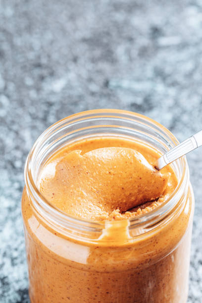 istock Spoon dipping into a glass jar with crunchy peanut butter. 1336655547