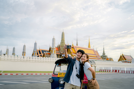 Two Asian tourists use their smartphones as they stand in the middle of the road and have fun taking pictures around popular spots.
