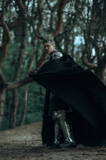istock Medieval knight in armour and black cape stands in forest. 1336658081