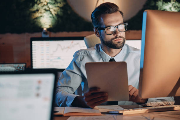 Confident young man working on computer Confident young man working on computer while staying late in the office formal businesswear stock pictures, royalty-free photos & images