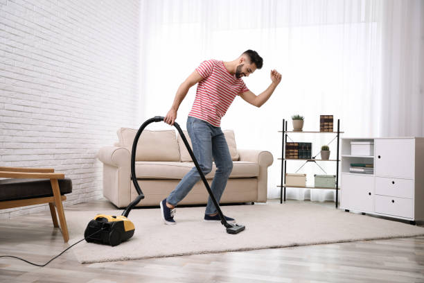 istock Young man using vacuum cleaner at home 1336663216