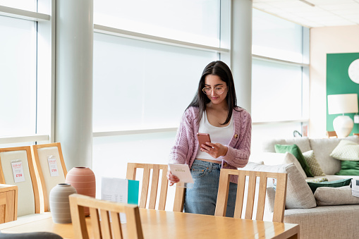 A young girl in a furniture store, taking a picture of furniture prices on point of sale with her mobile phone.