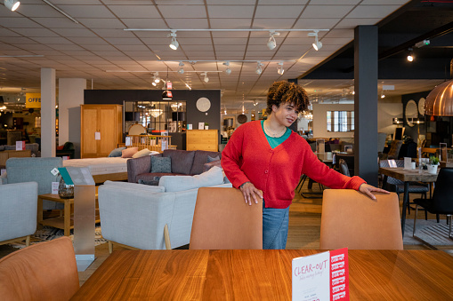 A mid adult woman shopping in a furniture store, examining and touching a dining table, she is thinking about buying it. The table is at a reduced price.