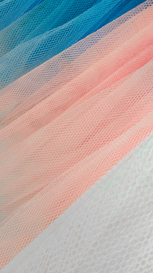Fragment of multicolored ballet tutus.Abstract close-up selective focus pink and blue mesh diagonally.Folds and curls of fabric in small stitch.Vertical banner,wall paper,textured background.