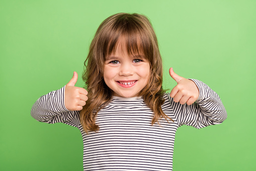 Photo of funny little blond hair girl show thumb up wear striped shirt isolated on green color background.