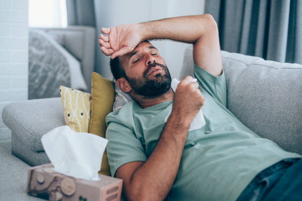 Man with high fever at home. Sick young man lying on the couch and blowing his nose. Ill man lying on the sofa with high temperature. man fever stock pictures, royalty-free photos & images