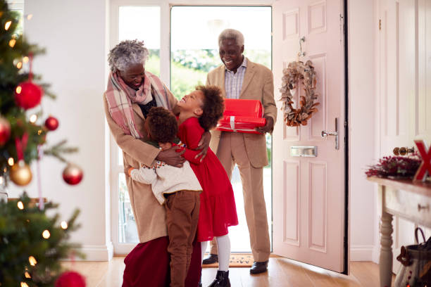grandchildren greeting grandparents as they arrive with presents to celebrate christmas - family christmas imagens e fotografias de stock