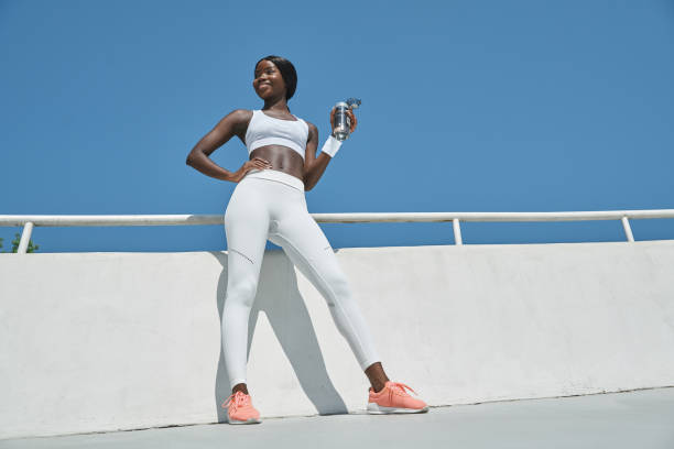 Low angle view of beautiful young African woman in sports clothing holding bottle with water