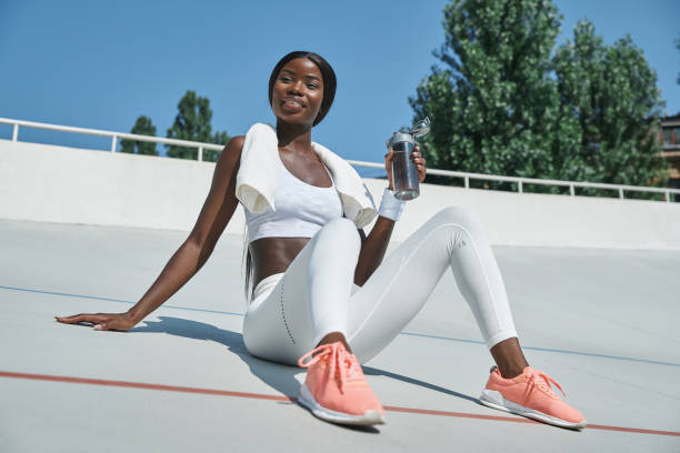 Beautiful young African woman in sports clothing holding bottle with water