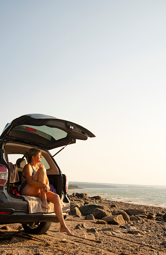 A mature woman sitting in the back of her car at the beach