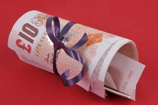 Roll of sterling banknotes in close-up on a red background