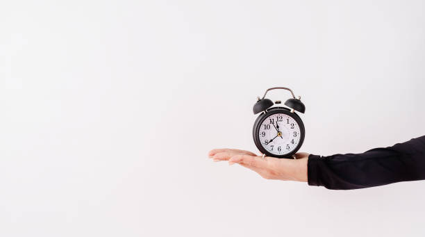 istock Female hand holding white alarm clock on white background 1336680888