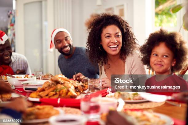 Multi Generation Family In Paper Hats Enjoying Eating Christmas Meal At Home Together Stock Photo - Download Image Now