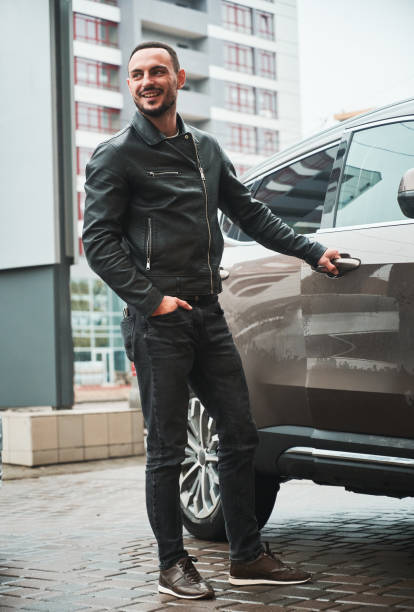 Full length shot of handsome smiling man posing near his modern car outdoor.