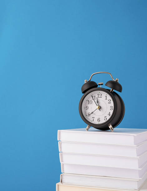 istock Black alarm clock on stack of books on blue background, mockup design 1336682202