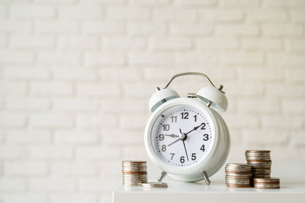 istock White retro alarm clock with coins on white brick wall background 1336682262
