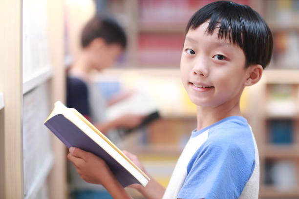 istock Happy Asian kid reading book in library 1336686247