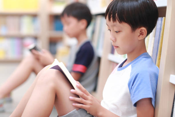 istock Happy Asian kid reading book in library 1336686253
