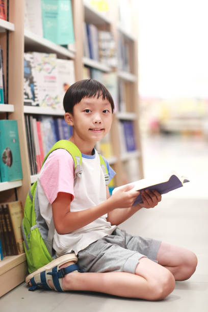 istock Happy Asian kid reading book in library 1336686271