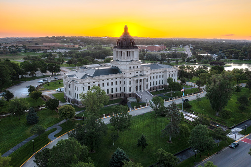 Aerial photo of the Capitol building in Pierre, South Dakota at sunrise. Drone shot looking down from a high angle towards the historical white statehouse with golden sky in background.