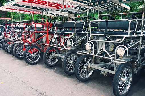 Row of vintage pedal-power four-wheeled surrey bike for rent on parking in public park. Rental station of retro quad bikes. Ecofriendly street transport, healthy lifestyle, urban environment