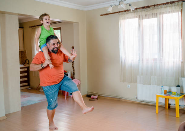 little son sitting on father's shoulders and having fun,little preschool kids to dance in modern living room at home. - family large american culture fun imagens e fotografias de stock