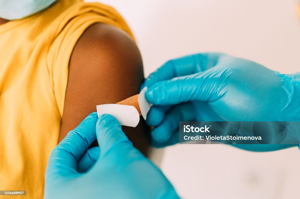 Doctor putting a bandage after Covid-19 vaccination. Male doctor putting a bandage on the arm of a little girl after giving Coronavirus/COVID-19 vaccine in the clinic. Close-up shot of a healthcare worker placing a bandage on a patient's arm after coronavirus vaccination. Vaccination Stock Photo