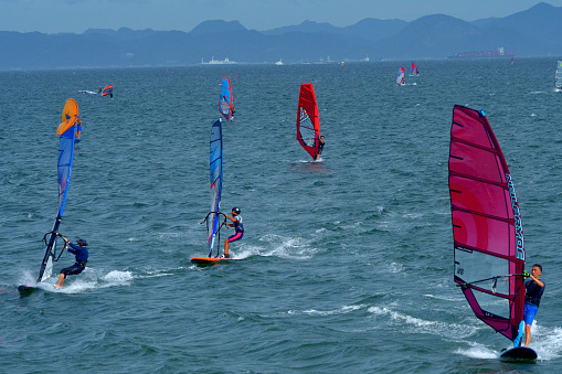 Young girl pulling a sail from the water before windsurfing in a blue ocean in a summertime.
