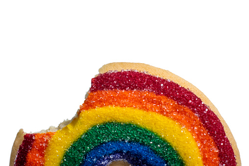Close Up of Decorative Rainbow Cookie on a white background. The granulated sugar sparkles in the light. There is a big bite taken out of the cookie.
