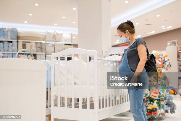 Pregnant Woman In Protective Face Mask Choosing Baby Crib In A Store Stock Photo - Download Image Now
