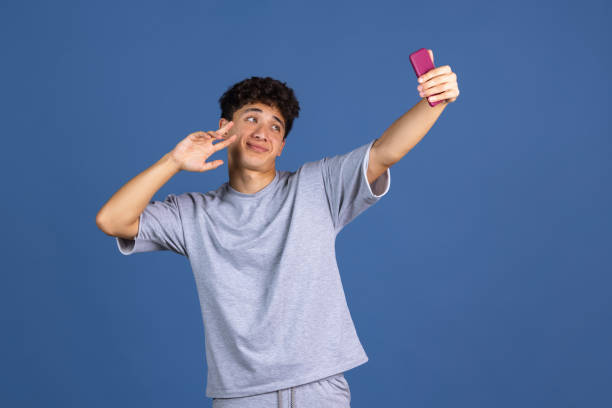 istock Portrait of young curly man using phone isolated over blue studio background with copyspace for ad. Concept of human emotions, fashion, beauty, youth 1336699450