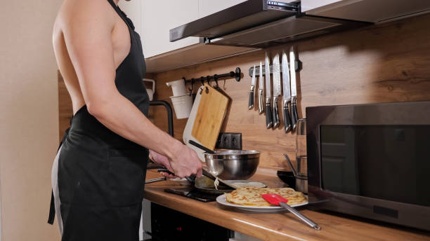 unkenntlicher mann mit nacktem oberkörper und in schwarzer schürze bereitet pfannkuchen in der küche zu - back somersault stock-fotos und bilder