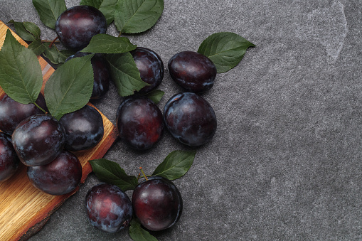 Fresh purple plums with leaves on stone table, top view, copy space.