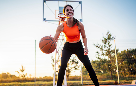 Young smiling woman bouncing the ball in a street basketball court