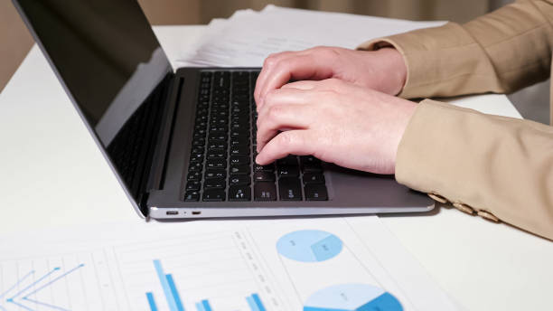 istock Hands type on laptop keyboard and brunette looks at graphs 1336706546