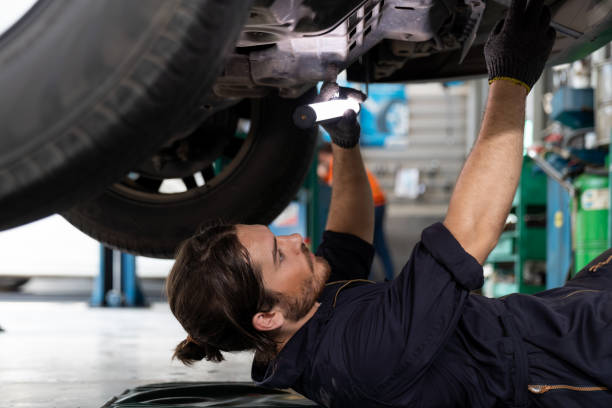 istock Male car mechanic worker working using wrench tool for repair, maintenance underneath lifted car. Mechanic vehicle service checking under car in garage. Auto car repair service, maintenance concept 1336708122