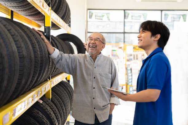 autoservice. asiatische verkäufer empfehlen neue reifenräder im regal regal für ältere kunden in der autowerkstatt. fachmechaniker und kunde bei der prüfung des neuen reifenrades - mechanic auto repair shop manual worker men stock-fotos und bilder