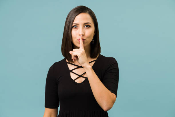 Portrait of a woman asking for silence Don't say anything. Beautiful young woman putting a finger on her lips and asking to keep a secret whispering stock pictures, royalty-free photos & images