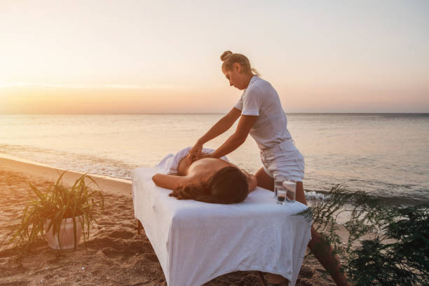Young masseuse doing massage by the sea at sunrise A young masseuse in white clothes makes a massage on the seashore at dawn. Massage table on the seashore at sunrise. dorsal fin stock pictures, royalty-free photos & images