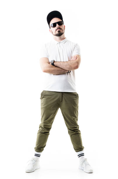 Cocky confident attitude stylish young man posing with crossed arms wearing cap and sunglasses. Cocky confident attitude stylish young man posing with crossed arms wearing cap and sunglasses. Full length portrait isolated on white background olive green shirt stock pictures, royalty-free photos & images