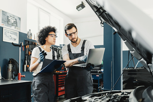 Car Mechanic Use Notebook Computers to Check Engine and Service Maintenance in a Car Service Garage