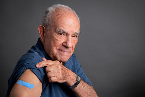 Senior man posing showing his vaccination band-aid in his arm looking at the camera