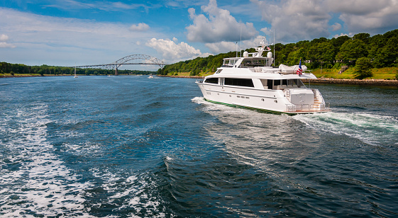 A large white luxury yacht travels west on the Cape Cod Canal  toward the Bourne Bridge on a warm August morning.