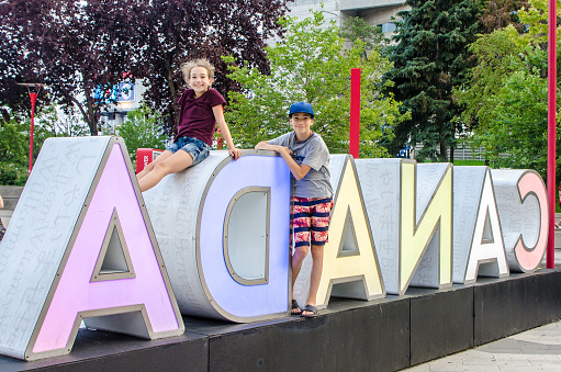 Girl and boy standing and sitting on the illuminated reversed word Canada in Toronto during summer day