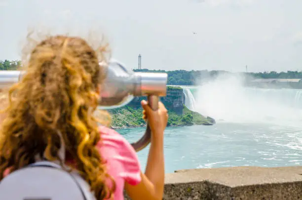 Girl looking at Niagara falls through paying binoculars during summer day from Canadian side