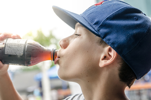 Side view headshot of boy drinking cola during hot summer day