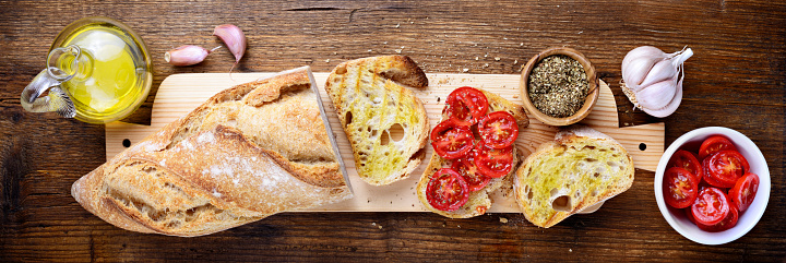 Mediterranean food, bread, olive oil, tomato and flavorings on wooden background, flat lay.
