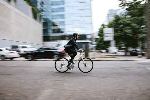 A Caucasian business man wearing a blazer rides his bicycle through the city streets of Seattle, Washington, USA.  He carries work items in a messenger bag slung over his shoulder.   An environmentally friendly and healthy way to commute to work: sustainable lifestyle.  A panning shot to convey speed and action.